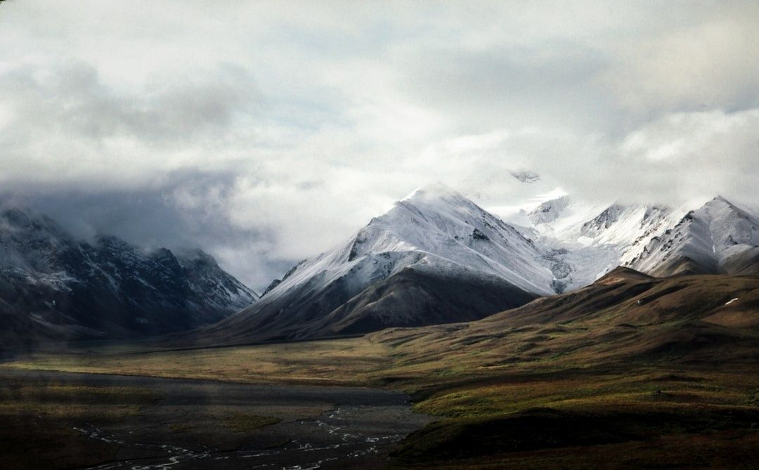 Snow-covered mountains rise above a broad tundra valley under clouds
